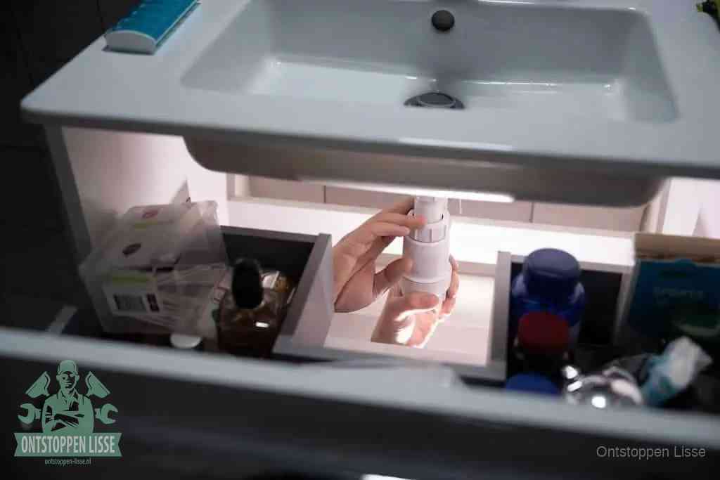 Een pompfles met zeep boven een wastafel, de heet water en afwasmiddel-methode om een vetprop in de afvoer los te maken in Lisse