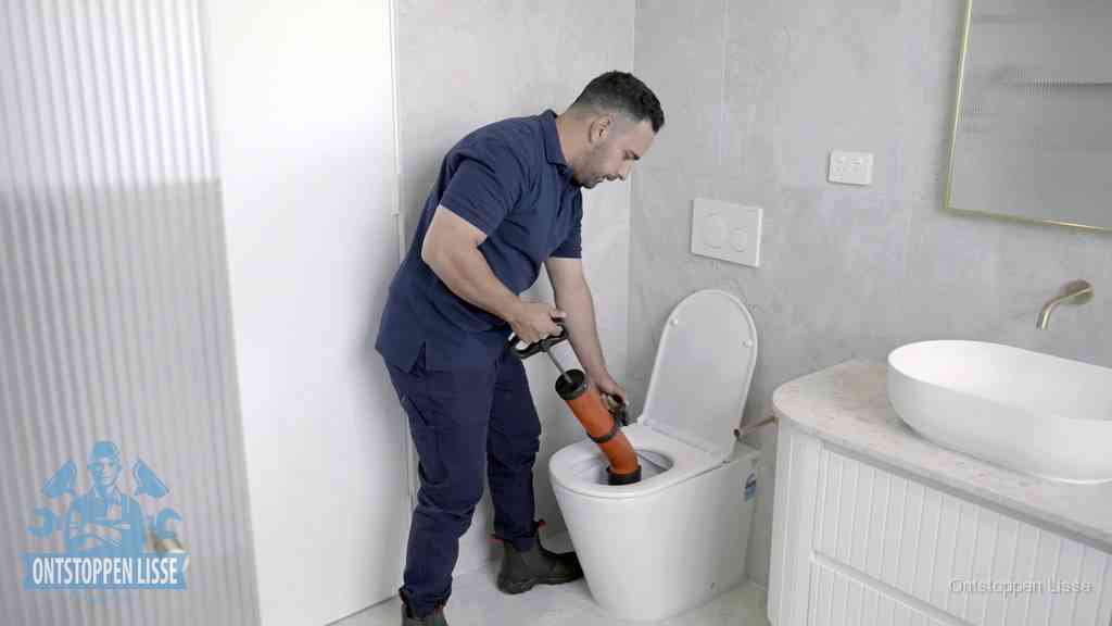 Een monteur buigt over een wandcloset en duwt met de hand een persluchtontstopper in de toiletpot om de verstopping handmatig los te maken in Lisse