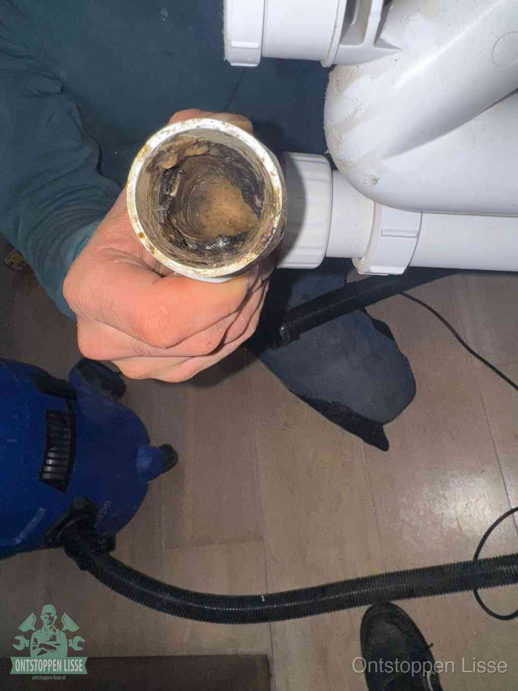 Een hand houdt een losgekoppeld PVC-afvoerbuisstuk vast dat van binnen volledig is dichtgeslibd met vet, vuil en aanslag, de meest voorkomende oorzaak van een verstopte afvoer in Lisse