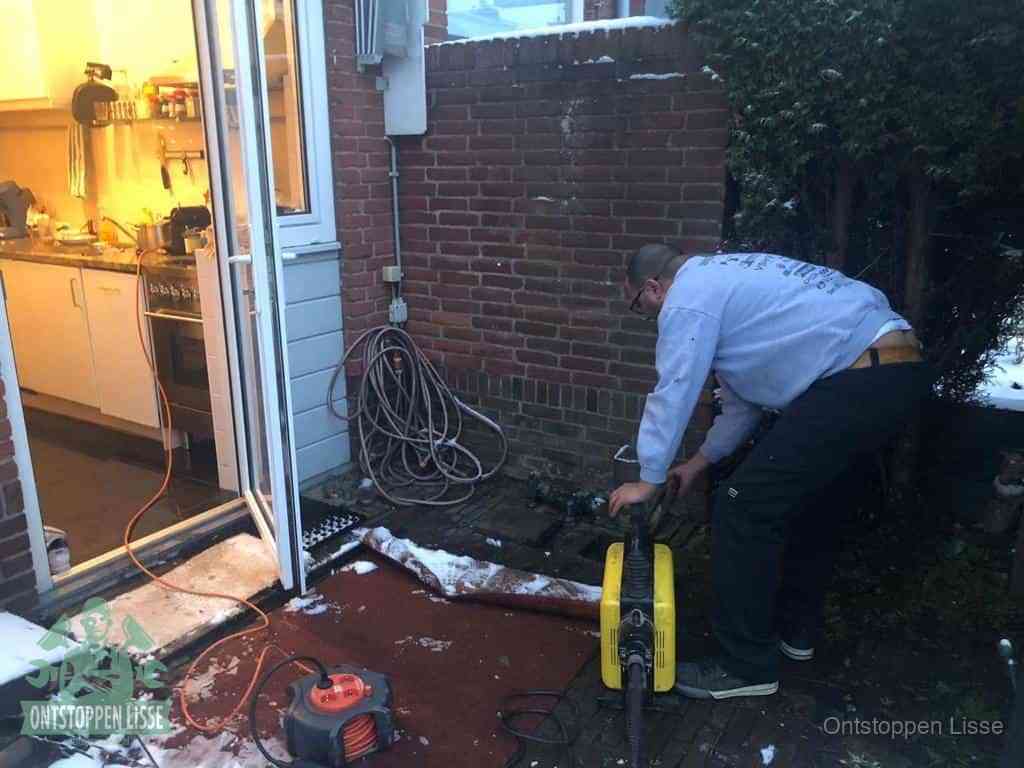 Een monteur werkt buiten bij een open riool-/grondput met een elektrische ontstoppingsmachine om een verborgen afvoerprobleem op te sporen in Lisse