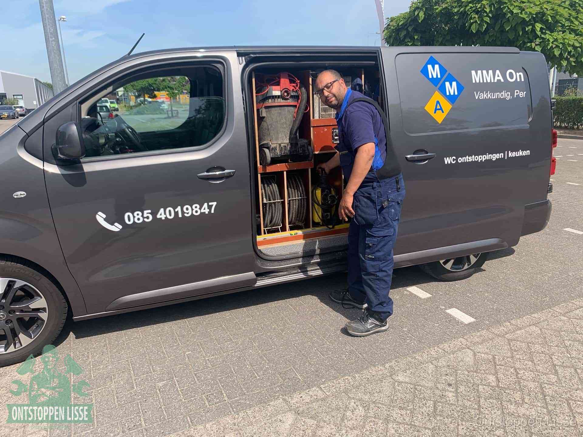 Een monteur bij de open schuifdeur van zijn bedrijfsbus op een parkeerplaats, klaar om de oorzaak van terugkerende afvoerverstoppingen aan te pakken in Lisse