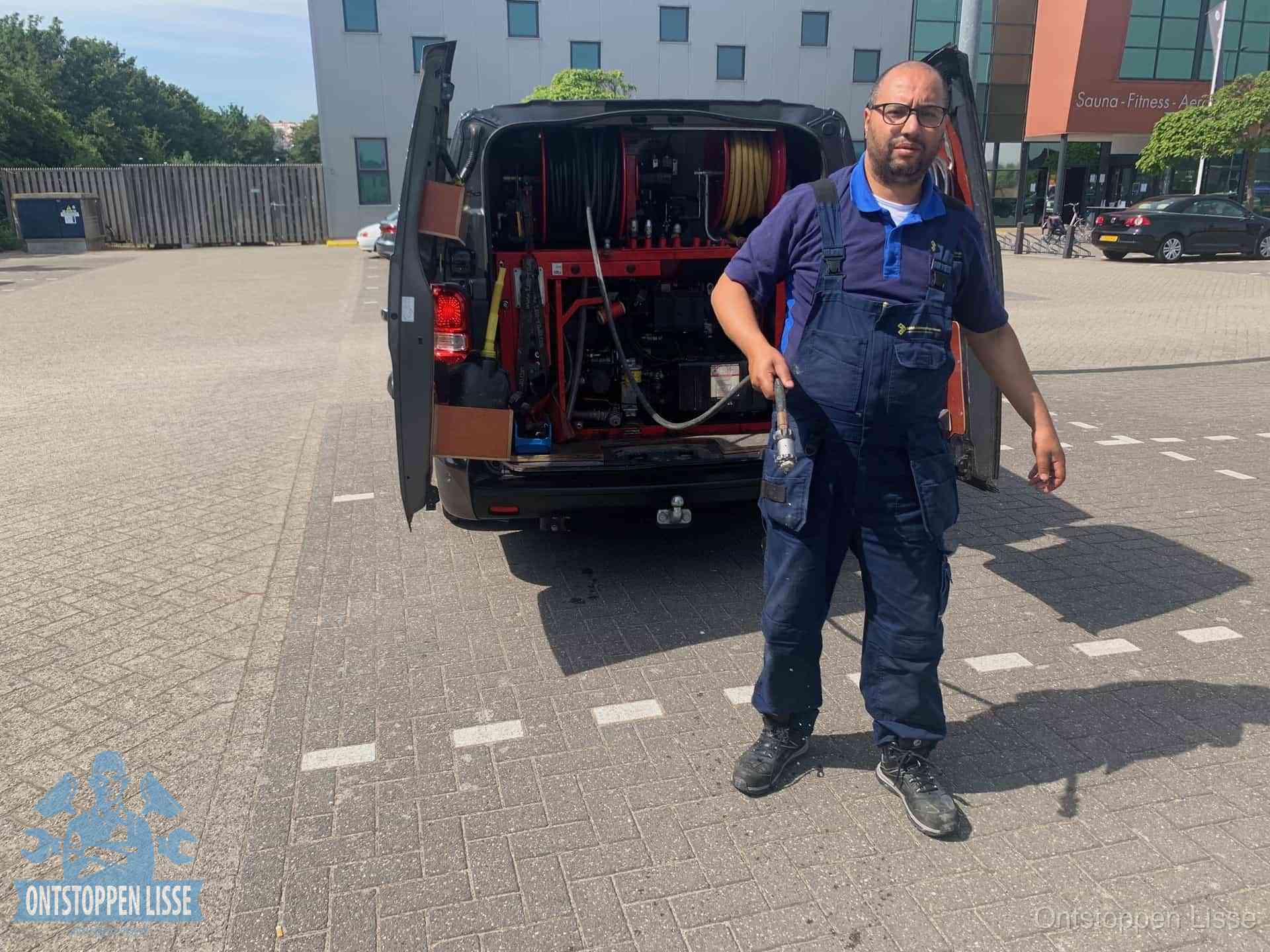 Een monteur bij zijn bestelbus met een hogedruk- en rioolreinigingsunit, klaar om de oorzaak van terugkerende wc-verstoppingen aan te pakken in Lisse