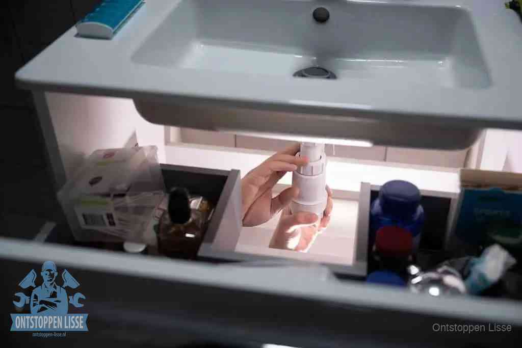 Een pompfles met zeep boven een wastafel in de toiletruimte, de warm water en afwasmiddel-methode om de wc te ontstoppen in Lisse