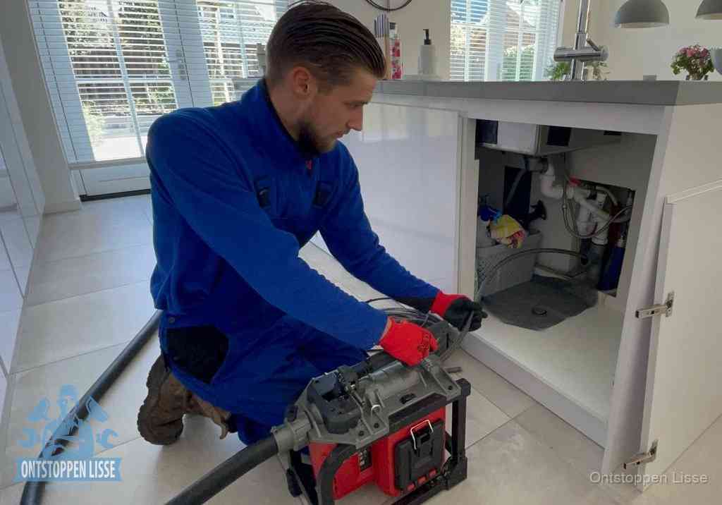 Een monteur voert een professionele elektrische ontstoppingsmachine in de afvoer onder de spoelbak tijdens het gootsteen ontstoppen in Lisse