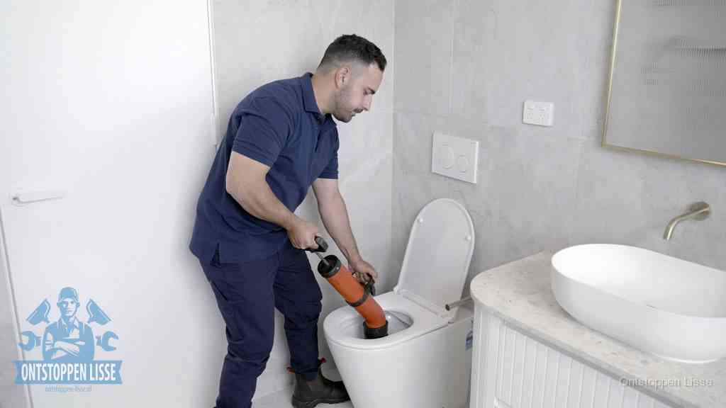 Een monteur gebruikt een handmatige perspomp (toiletontstopper) op een wandcloset tijdens het professioneel wc ontstoppen in Lisse