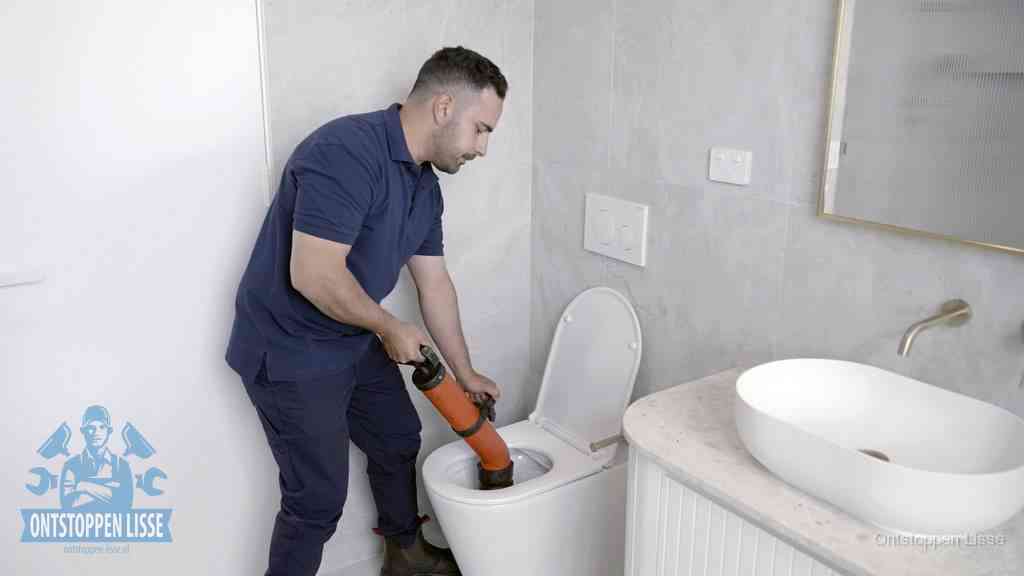 Een man gebruikt een handmatige luchtdruk-ontstopper in een modern betegeld toilet om zelf de wc te ontstoppen in Lisse